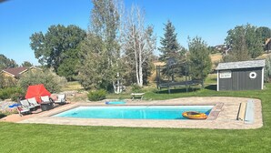 Ein Garten mit Schwimmbad, Trampolin und Gartenhaus.