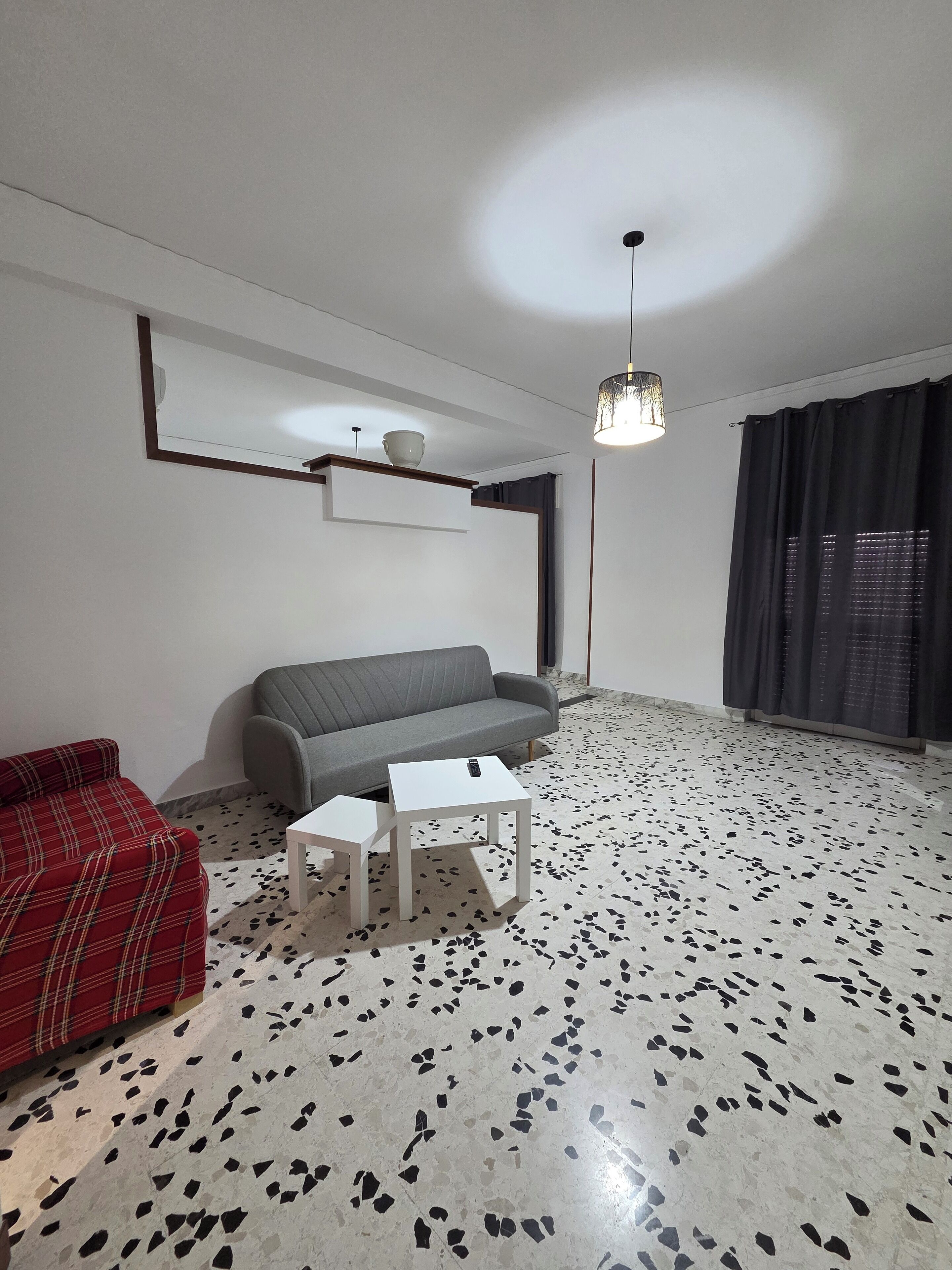 Un salon avec un canapé gris, un canapé à carreaux rouges, une table basse blanche et un sol noir et blanc à motifs.