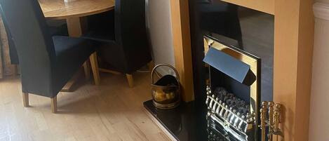 Un coin repas avec une table en bois et des chaises noires, un petit miroir rond, une horloge et un tableau encadré au mur.
