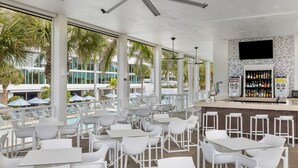 Een modern buitengebied met een bar, witte tafels en stoelen, en uitzicht op een zwembad. De bar is voorzien van diverse drankjes.