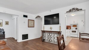 Amplia sala de estar con piso de madera, una mesa de comedor y una cocina con gabinetes y electrodomésticos blancos.