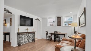 Una sala de estar con televisor, una mesa de comedor con sillas, un sofá de cuero y una lámpara.