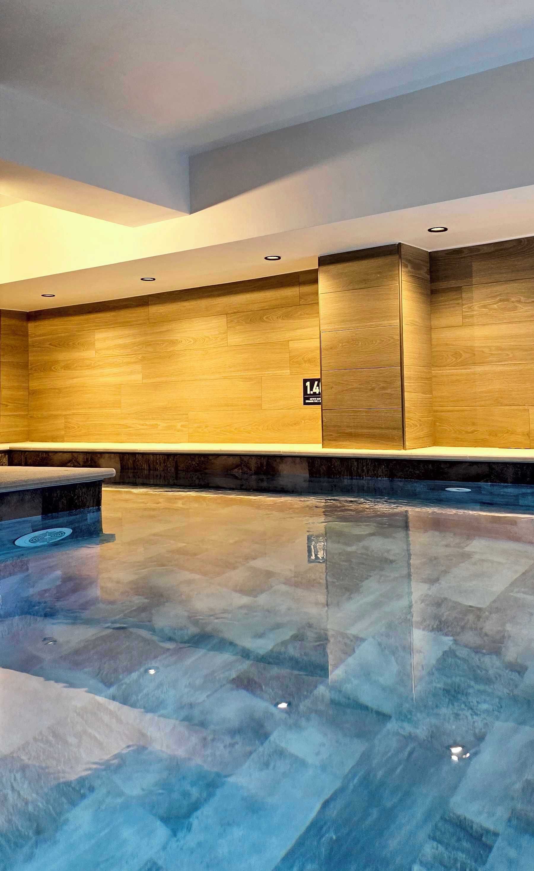 Un espace piscine intérieur moderne, avec un revêtement mural en bois et un banc.