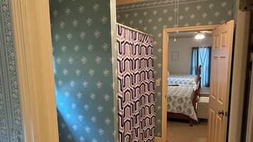 Un baño con inodoro, cortina de ducha y una cama visible a través de una puerta abierta.