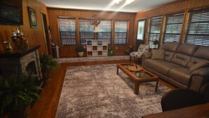 A living room with a fireplace, wooden floors, a sofa, a coffee table, and large windows with blinds.