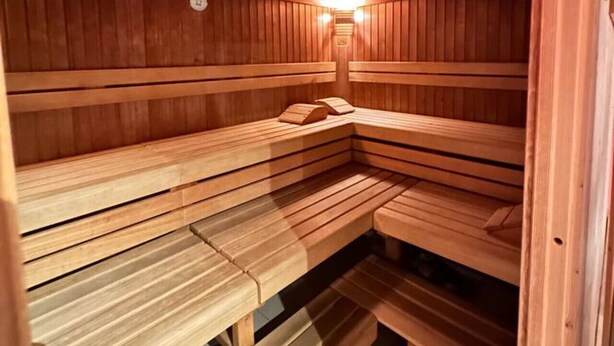 A wooden sauna with benches and a wall-mounted heater. - Gemütliches Apartment, Sauna, Nationalpark, Ruhe (Lindberg)
