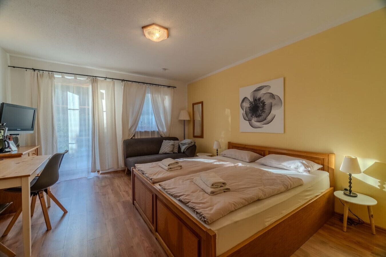 A hotel room with a bed, a desk with a computer, a chair, a sofa, and a lamp.