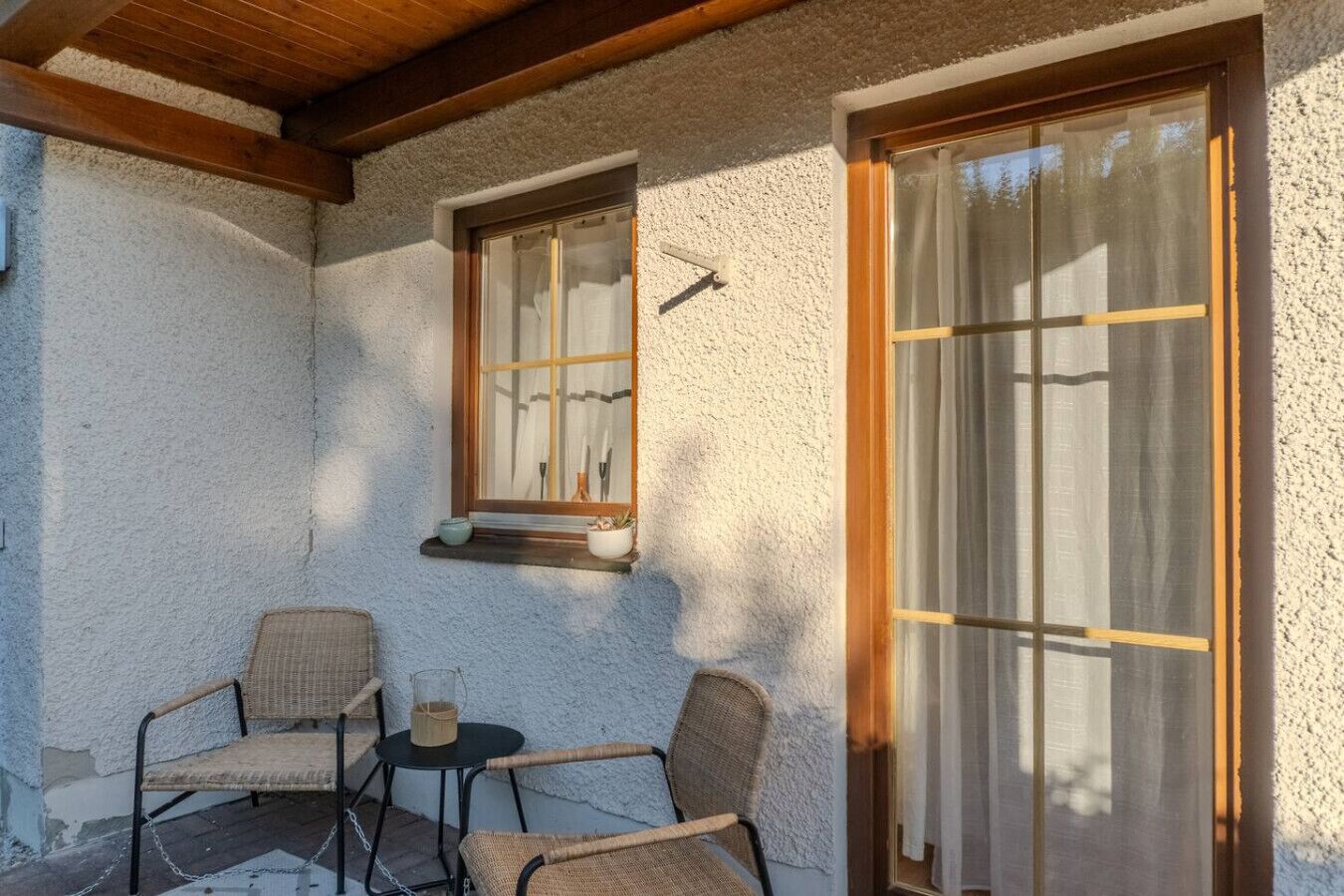 Een terras met rieten stoelen, een kleine tafel, een raam met houten kader en een structuurwand.