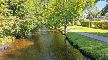 A clear water stream in a park with trees and a paved path.