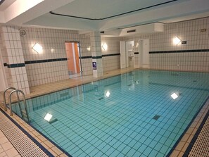 Una piscina interior con paredes y suelo de baldosas, y una puerta visible que da a otra habitación.