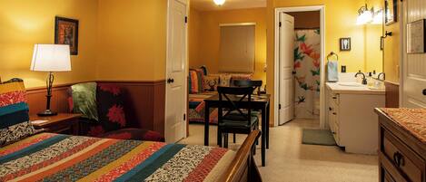 A bedroom with a bed, a desk, a chair, a dresser, and a bathroom with a sink and mirror.