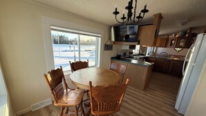 A dining area with a round wooden table and chairs, a chandelier, and a view of a snowy landscape through a large window.