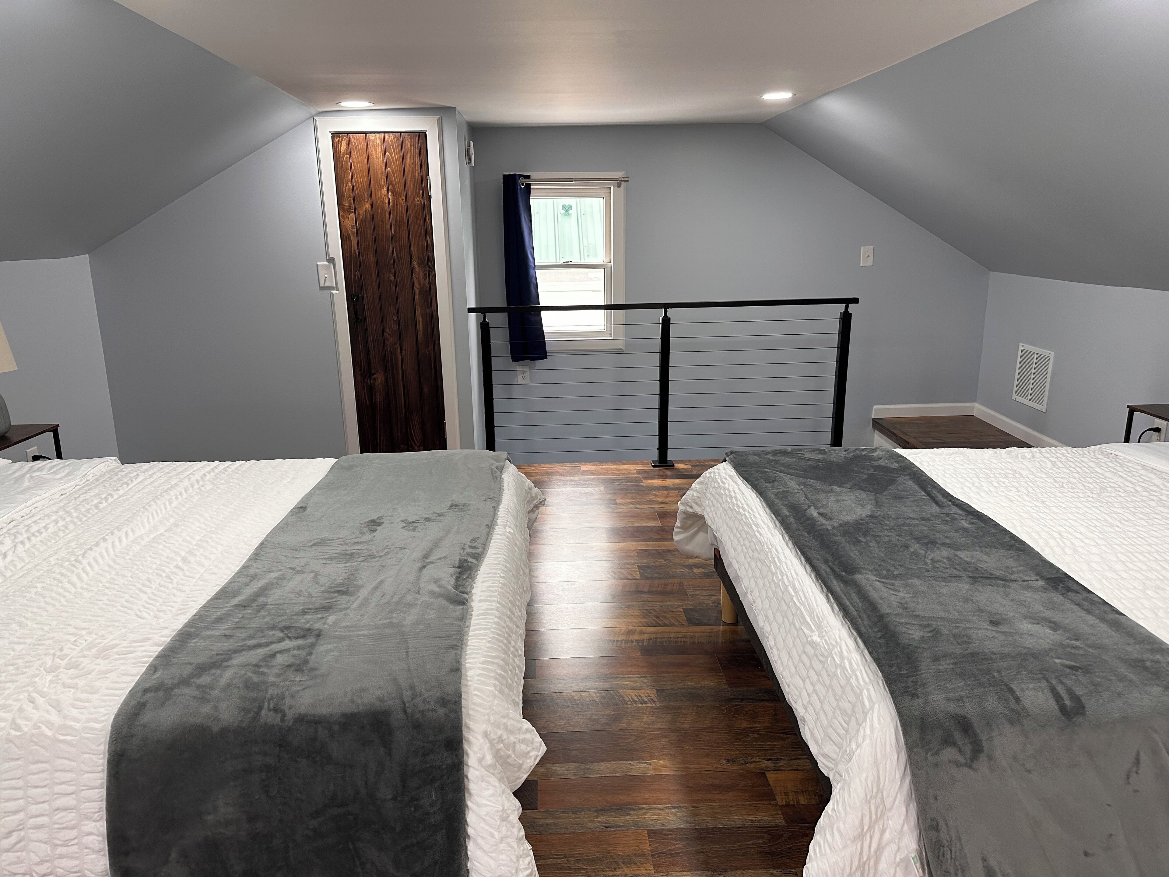 Un dormitorio con dos camas, suelo de madera, una ventana con cortinas y una puerta.