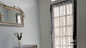 A room with a wooden floor, a white door with a patterned curtain, a small white vase with green plants on a wooden console table, and a mirror above the console. - Blue Getaway (Gettysburg)