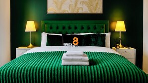 A hotel room with a green upholstered headboard, a bed with a green textured bedspread, two bedside lamps, and a pillow with the number 8. - Luxury Cinema Lounge 2Bed Leeds City Centre FREE Parking (Leeds)