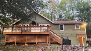 Ein Haus mit einer Holzterrasse, einer kleinen Veranda und einem überdachten Grillbereich.