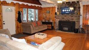 Ein gemütliches Blockhaus-Interieur mit Kamin aus Stein, Holzwänden, einer Couch und einem Fernseher.