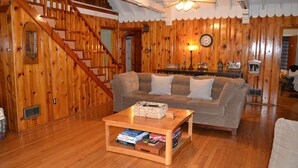 Ein Holzinterieur mit einer Couch, einem Couchtisch mit Büchern, einer Uhr und einer Treppe.