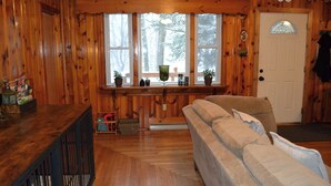 Ein gemütliches Blockhaus-Interieur mit Holzvertäfelung, einer Couch, einer Bank und einem Fenster mit Blick auf Bäume.