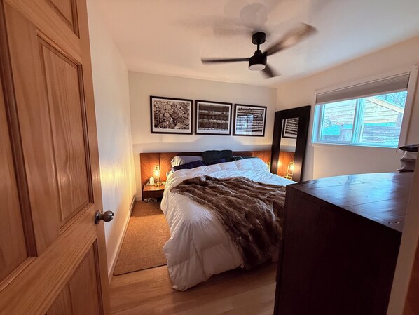 A bedroom with a bed, bedside lamps, a ceiling fan, and framed artwork on the wall.