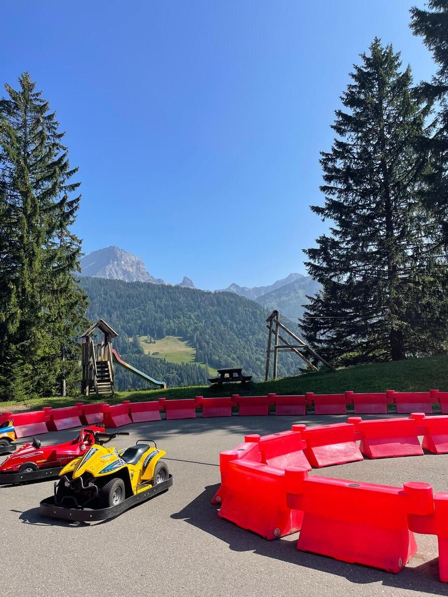 A go-kart track with red barriers, a wooden structure, and a mountain backdrop.