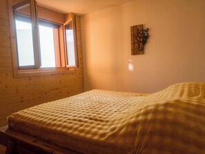 Ein Zimmer mit einem Bett, Holzwänden, einem Fenster und einem an der Wand hängenden Kunstwerk.