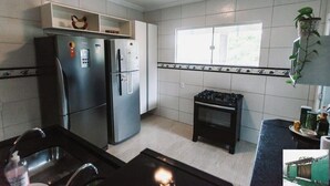 Een keuken met een koelkast, fornuis, spoelbak en raam.