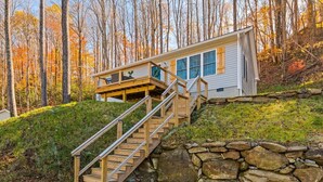 Una cabaña con una escalera de madera que conduce a una terraza, rodeada por un muro de piedra y un bosque.