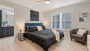 Un dormitorio con cama, una silla, una mesita de noche, un ventilador de techo y una ventana con persianas.