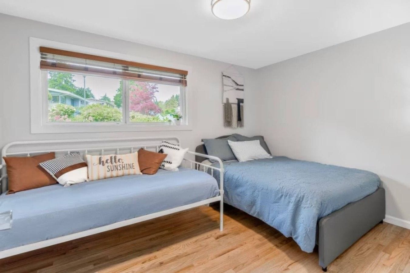 Une chambre avec deux lits, une fenêtre avec des stores, un luminaire au plafond et une vue sur la verdure.