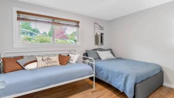 Une chambre avec deux lits, une fenêtre avec des stores, un luminaire au plafond et une vue sur la verdure.
