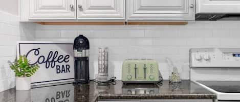 A kitchen with white cabinets, a coffee bar sign, a coffee maker, a toaster, and an oven.