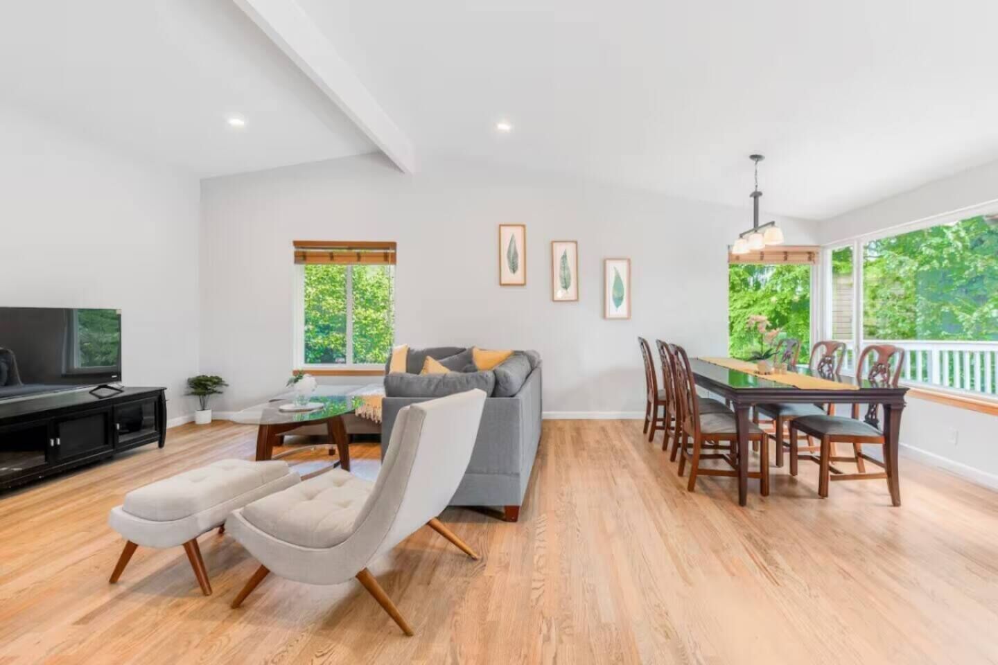 A spacious living area with a grey sofa, a dining table with chairs, a flat-screen TV, and a wooden floor.