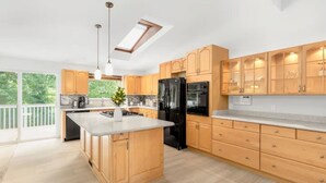 A modern kitchen with wooden cabinets, a central island, a black refrigerator, and pendant lighting. - Spacious 6BR/4BA | Close to Airport @South Seattle (Tukwila)