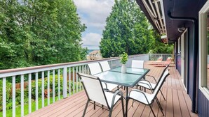 A deck with a glass table and chairs, surrounded by a white railing, overlooking a lush green landscape. - Spacious 6BR/4BA | Close to Airport @South Seattle (Tukwila)