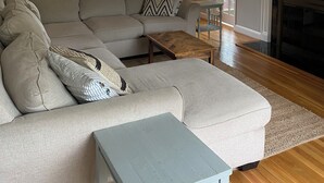 Un salon comprenant un canapé d’angle, une table basse, une cheminée et deux bibliothèques remplies de livres.