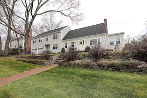 A two-story house with a stone pathway leading to the front door, surrounded by a well-maintained lawn and trees.