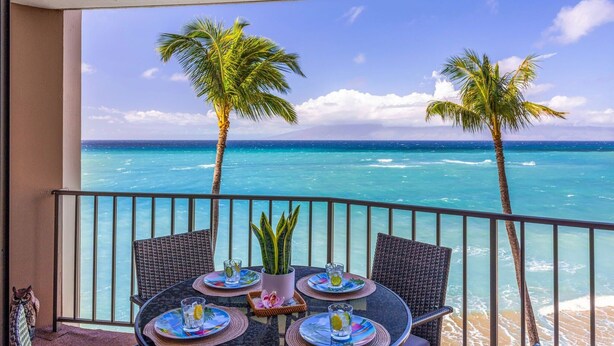 Ein Balkon mit Tisch für zwei Personen, mit Blick auf einen Strand mit Palmen und dem Meer.