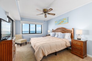 A bedroom with a bed, a chair, a nightstand, a television, and a ceiling fan. - Wake up to stunning ocean views in this beautiful Plaza condominium! (Ocean City)