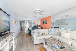 A modern living room with a large flat-screen TV, a sofa set, and a coffee table. - Wake up to stunning ocean views in this beautiful Plaza condominium! (Ocean City)