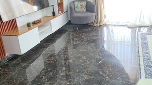 A modern living room with a flat-screen TV, a grey sofa, a wooden shelf with decorative items, and a marble floor.