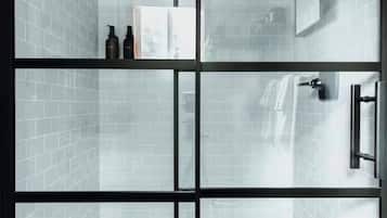A modern bathroom with a glass partition, a shower area, and a shelf with toiletries.