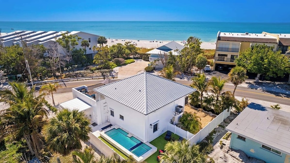 Una casa moderna y blanca con piscina, rodeada de palmeras y vistas a la playa.