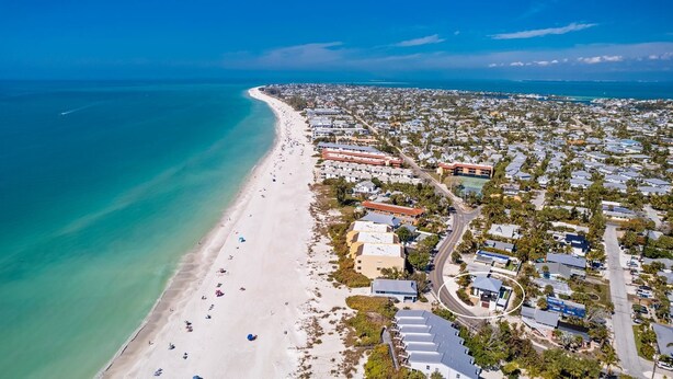 Vue aérienne d’une zone côtière comprenant une plage, des immeubles résidentiels et une route qui longe la côte.