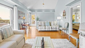 Un salon spacieux doté d’une grande fenêtre, d’un coin repas et d’un espace détente confortable avec un canapé et des fauteuils.