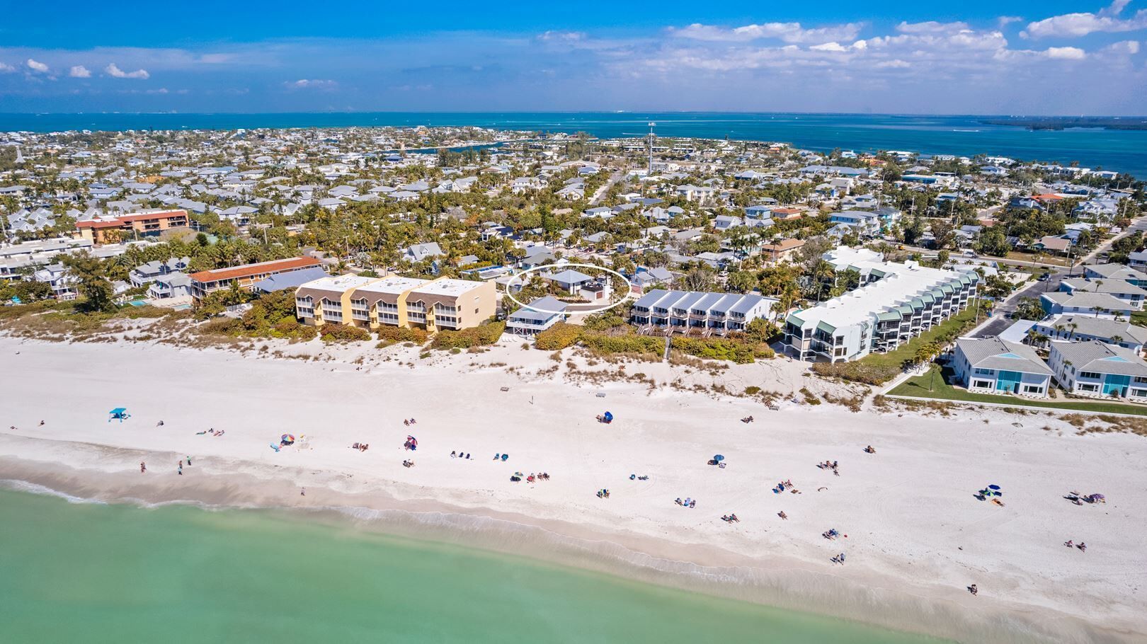 An aerial view of a coastal area with a beach, several buildings, and a marina.