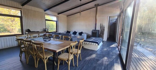 A cozy cabin interior with a wooden dining table, chairs, a sofa, and a fireplace.