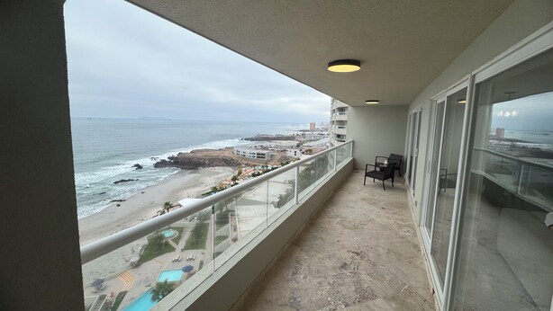 A balcony with a view of the beach and ocean, a pool, and a seating area. - The Pacibeach Condo - Oceanfront • Infinity View (Playas de Rosarito)