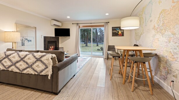 Ein modernes Wohnzimmer mit einer Couch, einem Kamin, einer Essecke mit Hocker und einer großen Weltkarte an der Wand.