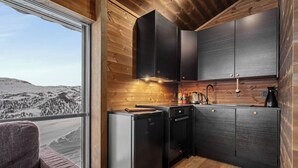 A compact kitchen with dark cabinets, a dishwasher, and a coffee maker. A window offers a view of a snowy landscape. - Exclusive cabin and annex at the top of Hodlekve (Vestland)